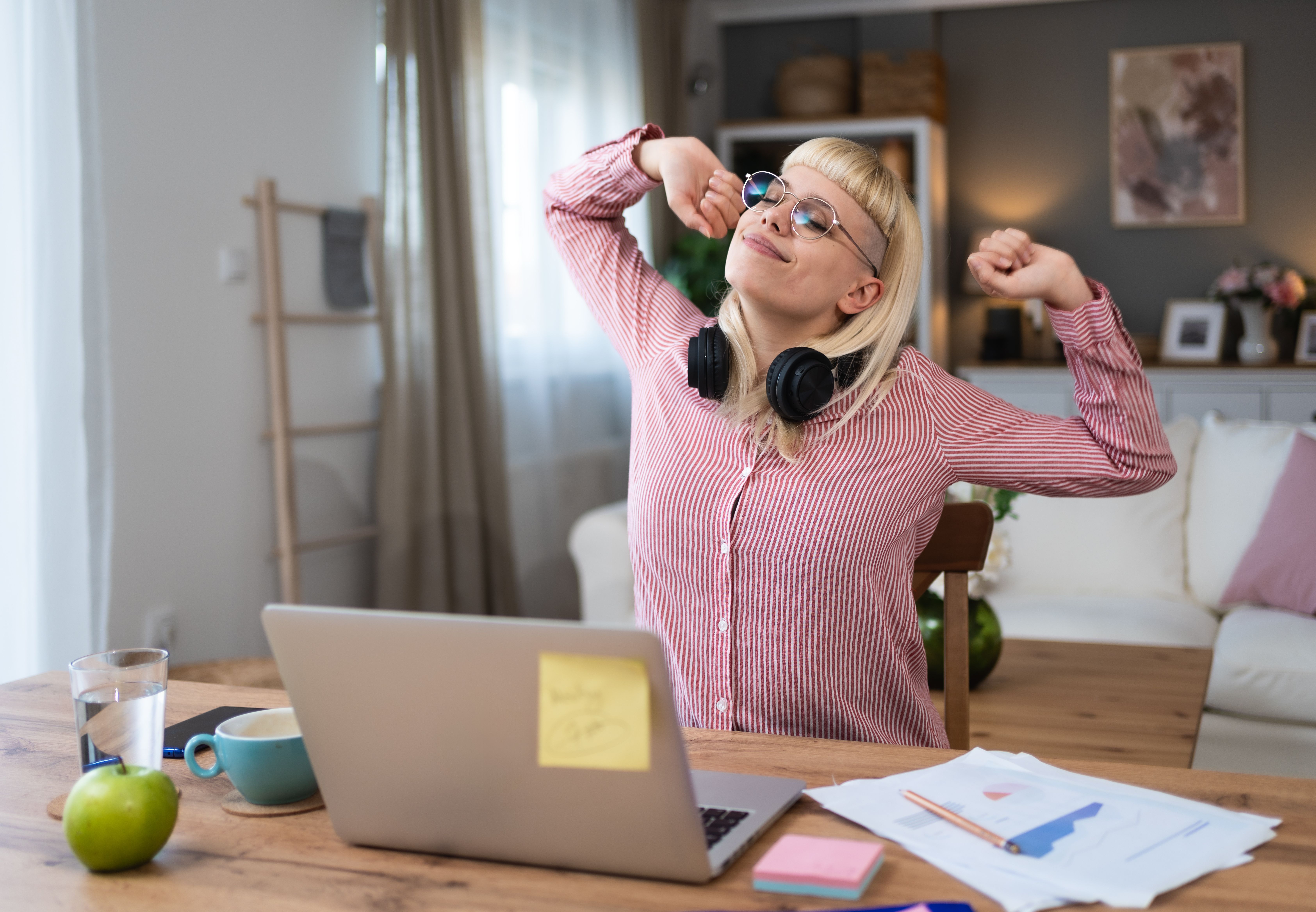 Frau am Schreibtisch vor Laptop streckt sich entspannt