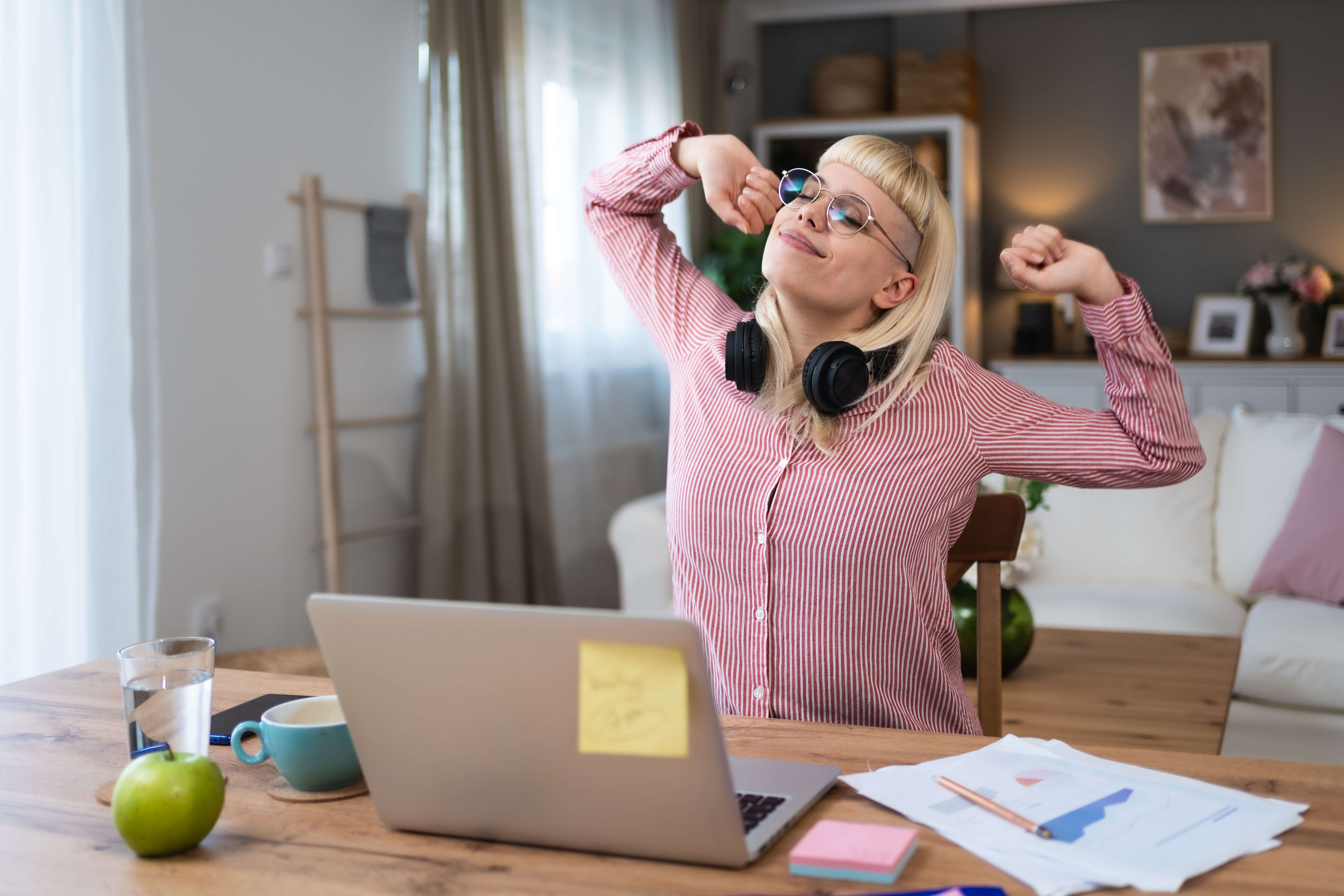 Frau am Schreibtisch vor Laptop streckt sich entspannt